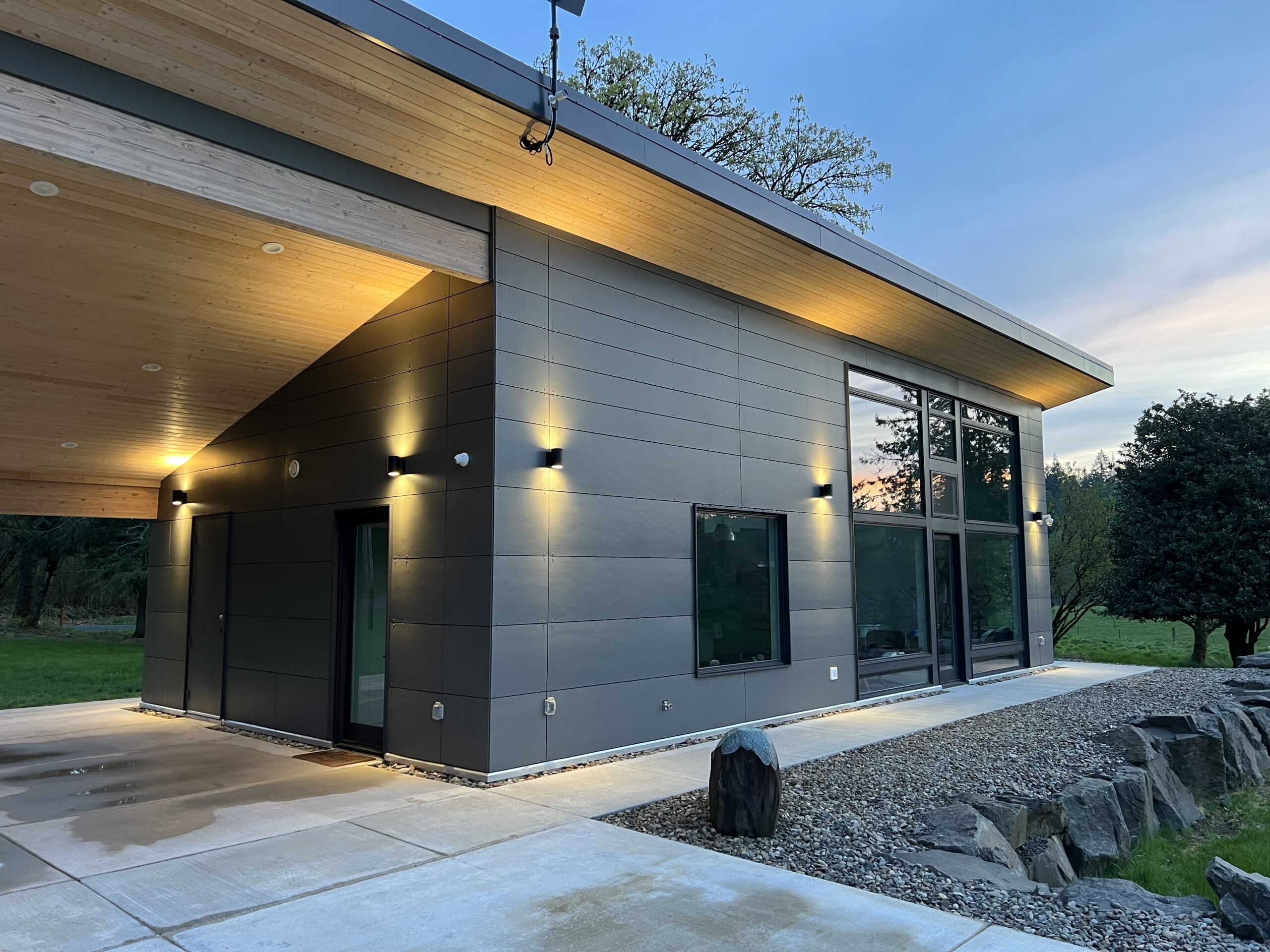 photo of a gray paneled modern residence and cement patio at dusk